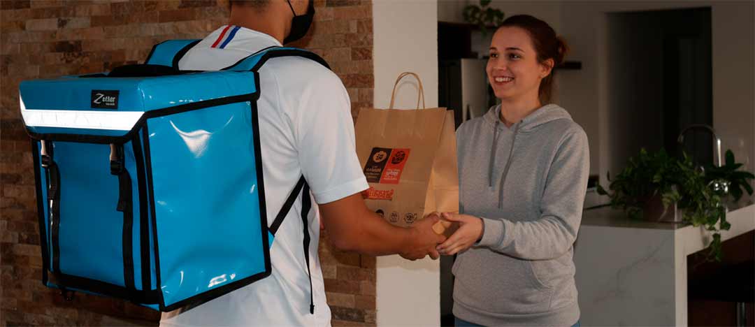 Repartidor con la mochila térmica pequeña JUNIOR azul cielo entregando un pedido